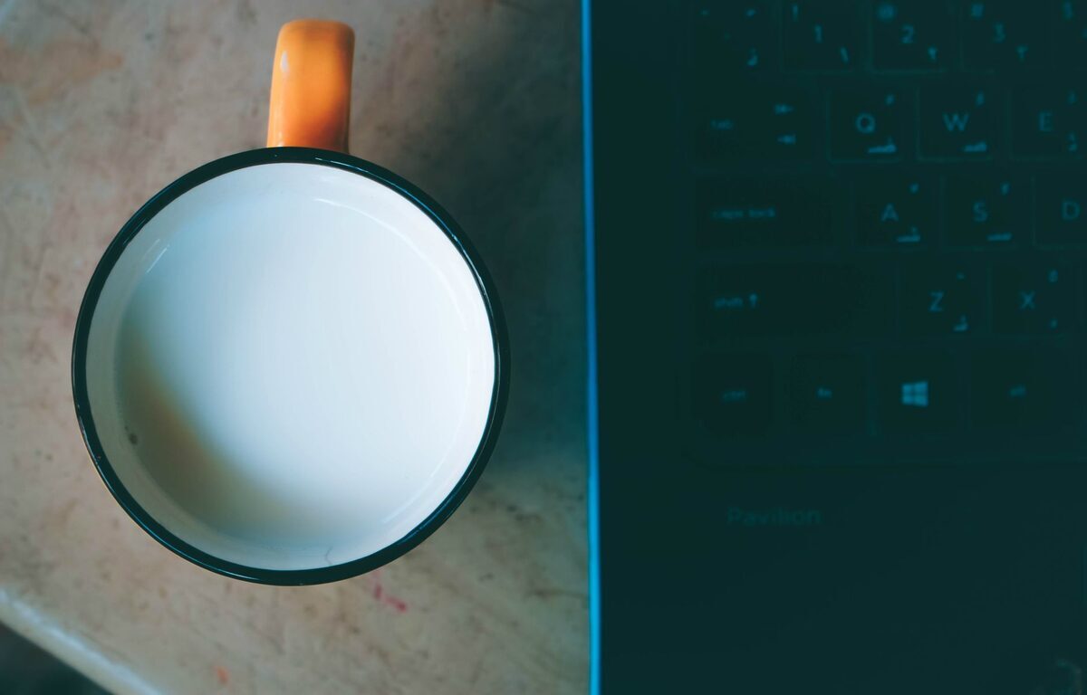 Kubek z mlekiem tuż przy otwartym laptopie — zalanie słodkim napojem a wodą