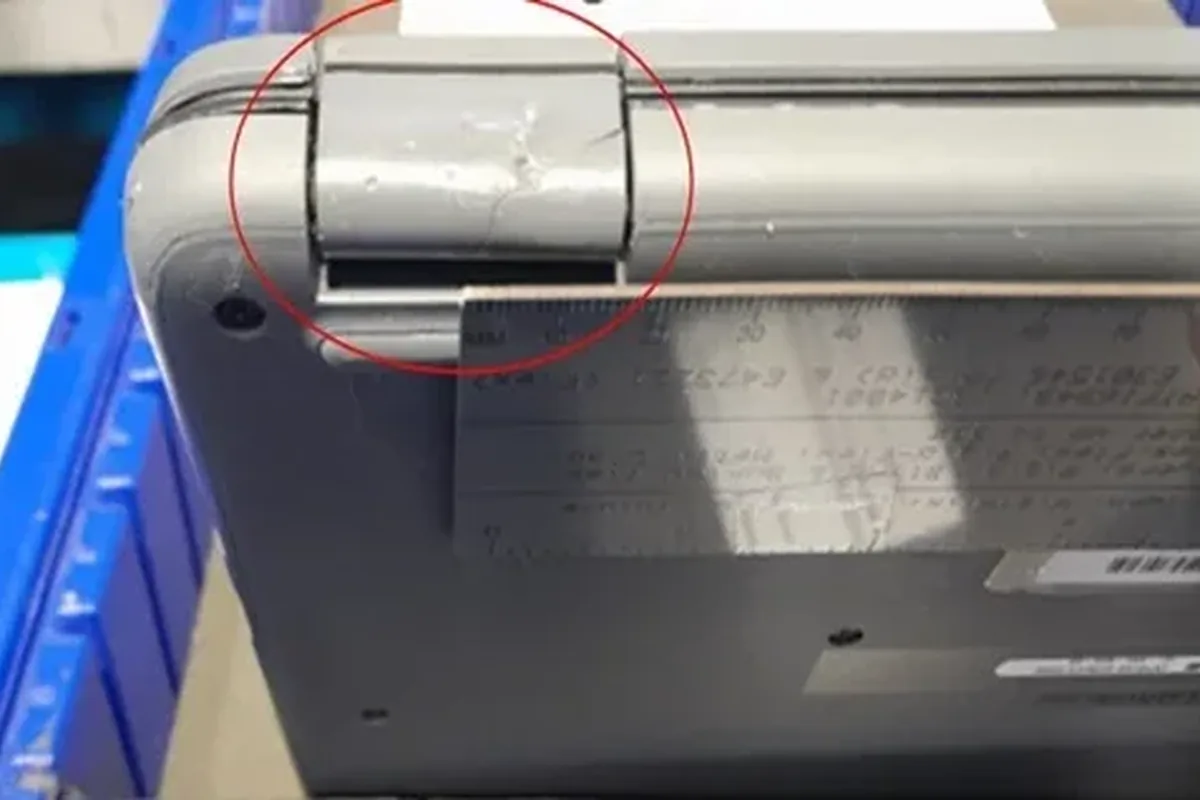 Zarysowany i pogięty zawias laptopa zaznaczony czerwonym kółkiem, laptop w magazynie